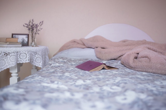Posteľ s farebnou obliečkou, na ktorej jej ružová deka a kniha