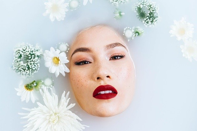 Žena ponorená vo vode mliečnej farby obklopená kvetmi.jpg